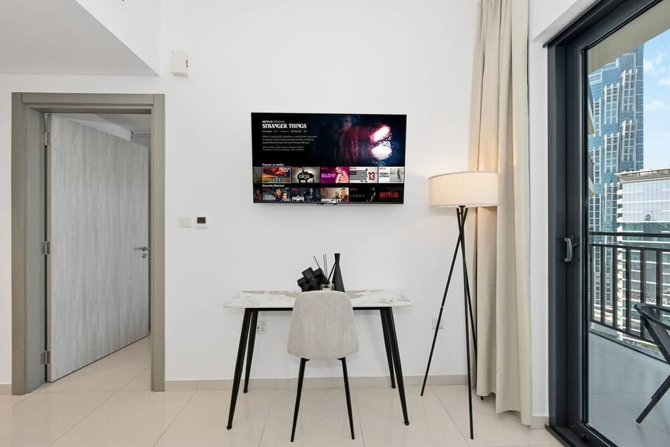 Bright and modern living space with a sleek open-plan design. The kitchen features light cabinetry and a marble-style dining table, flowing into a cozy lounge with balcony views of the city skyline. A separate bedroom adds comfort and privacy.