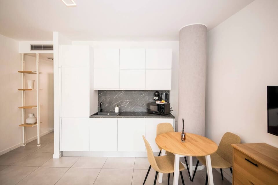 Bright kitchenette with white cabinets, marble-effect backsplash, coffee corner and cozy dining table.
