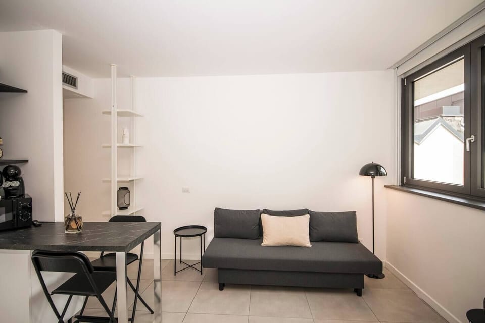 Bright kitchenette with marble-effect countertop, white cabinets, dining bar, black stools and Smart TV nearby.
