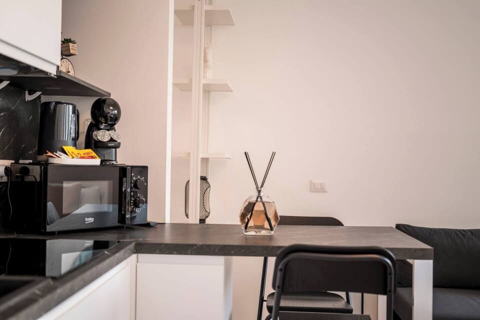 Modern fully equipped kitchenette with white cabinets, marble-effect backsplash, dining table, microwave and coffee machine.
