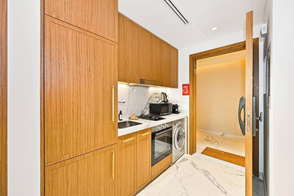 Modern brand-new kitchen with warm wooden cabinets, marble backsplash, and full amenities — including oven, washing machine, microwave, kettle, and Nespresso coffee maker — designed for a stylish and comfortable stay.