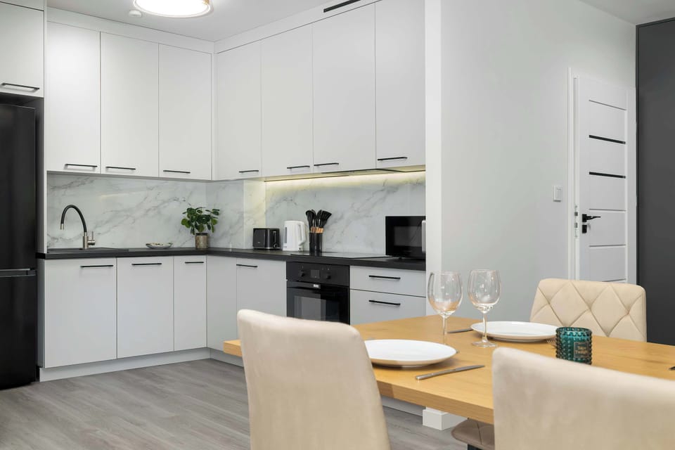 A modern kitchen and dining space with a wooden table prepared for a meal. White cabinets, built-in appliances, and light wood accents create a cohesive interior.