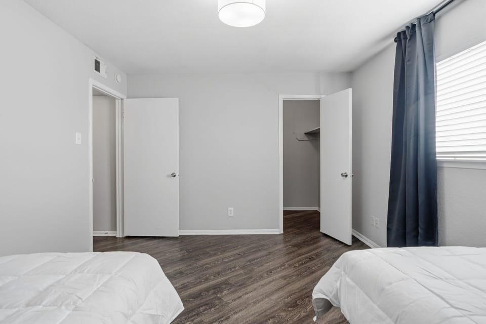 Bright bedroom with two beds, dark wood-look flooring, and navy curtains framing the window.