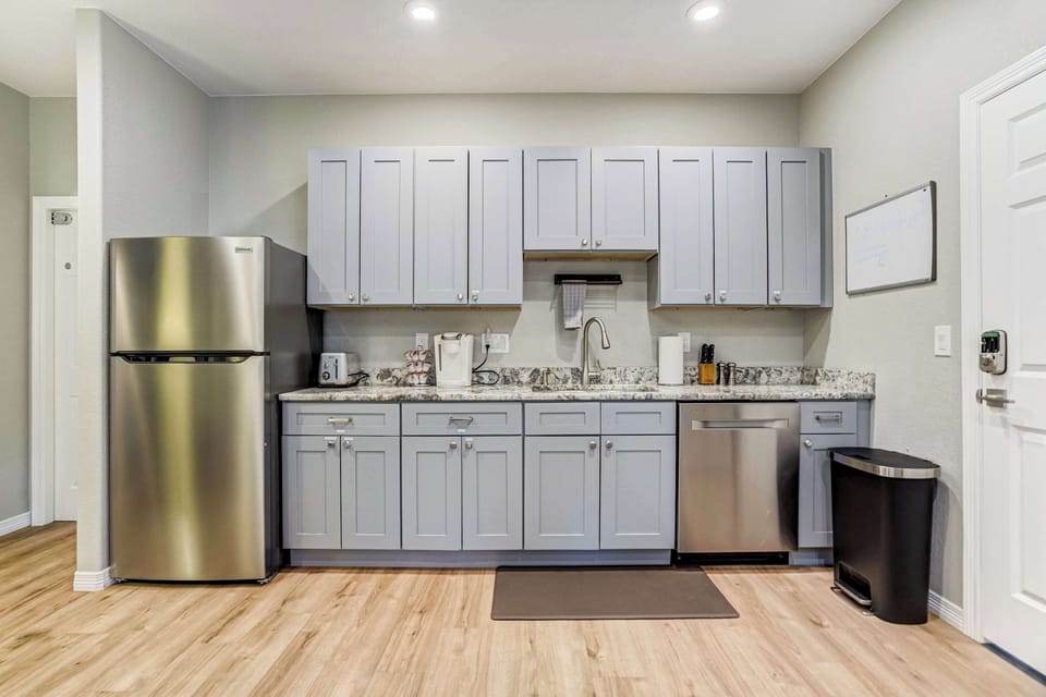 Speckled granite counters run the length of the kitchenette, paired with gray shaker cabinets and brushed hardware. A full size refrigerator, dishwasher, and complimentary coffee station with pods keep essentials close by.