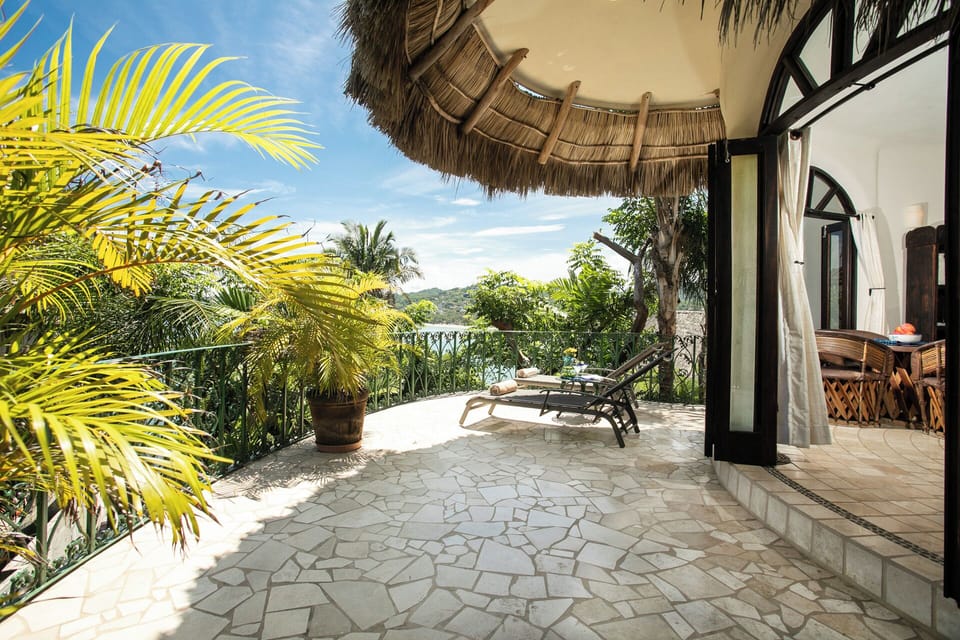 Palapa-shaded wide stone terrace with lounger, potted palm, and jungle bay view