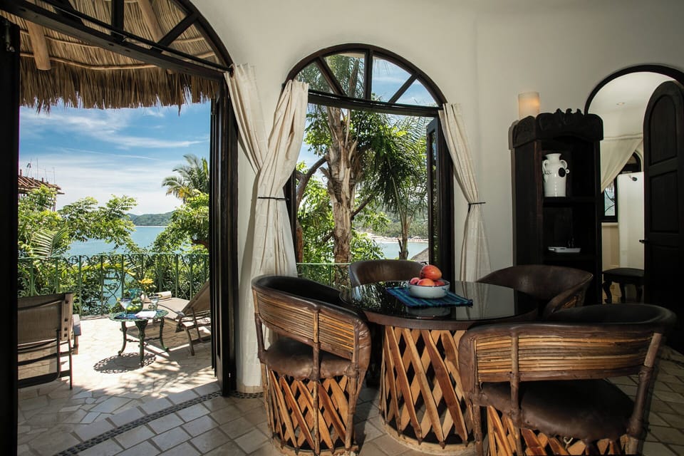 Dining set beside arched bay-view window and open terrace door to ocean