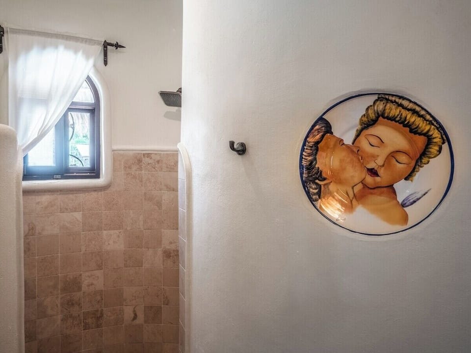 Bathroom with travertine walk-in shower, arched garden window, iron curtain rod, and hand-painted ceramic wall plate
