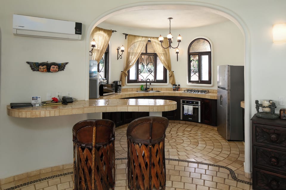 Curved full kitchen with tile breakfast bar, bamboo stools, arched windows, and chandelier