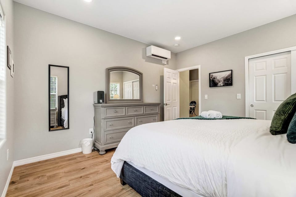 A tall dresser with a leaning mirror gives this king room generous storage, and its own mini split lets you dial in the temperature overnight. Neutral walls and warm hardwood floors keep the whole space calm and uncluttered.