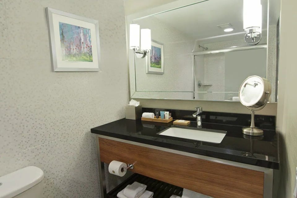 A bathroom with a white toilet, a sink with a mirror, and a shelf with towels.