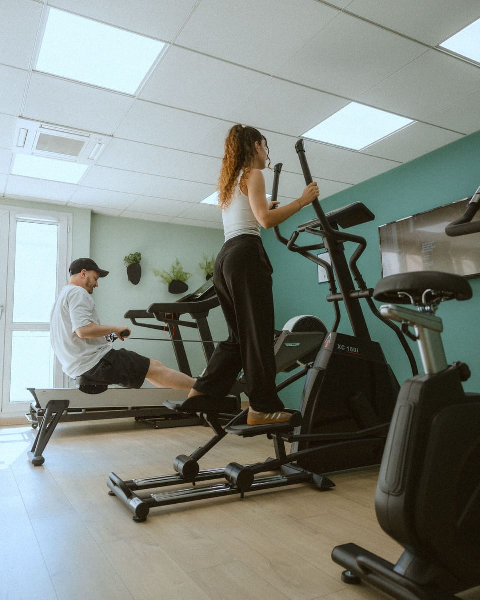 Woman on elliptical and man on rowing machine in fitness room.