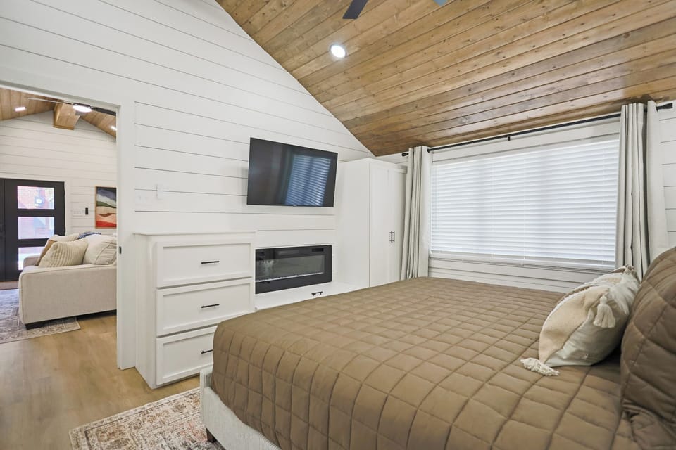 Cozy vaulted bedroom with fireplace, TV, and warm wood ceiling
