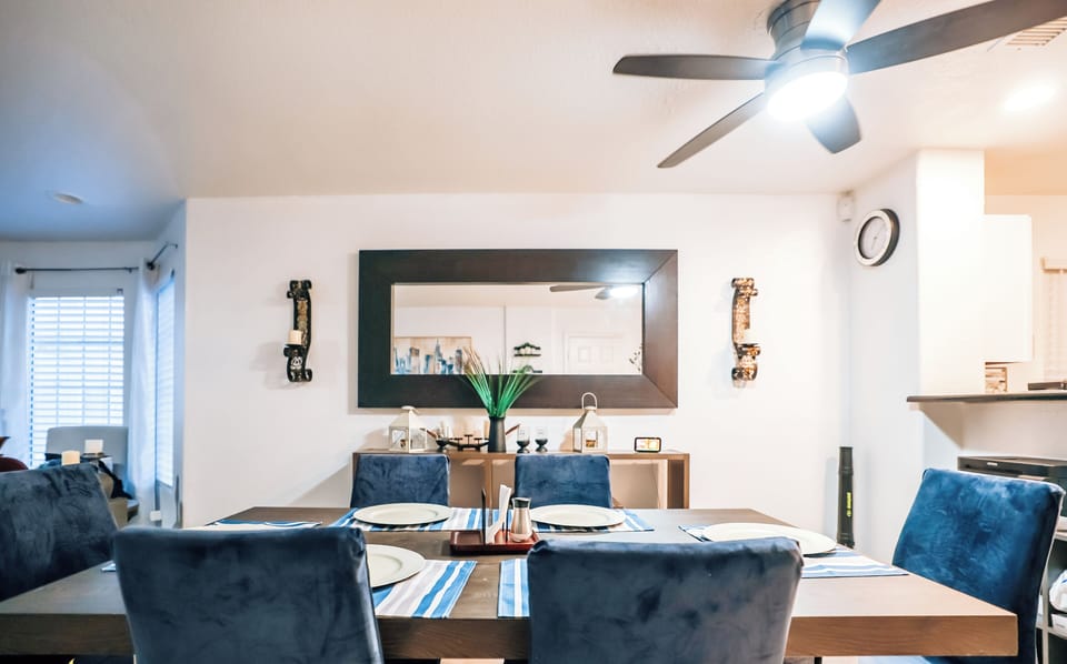 Bright dining for six with chic blue chairs, large mirror, and ceiling fan.