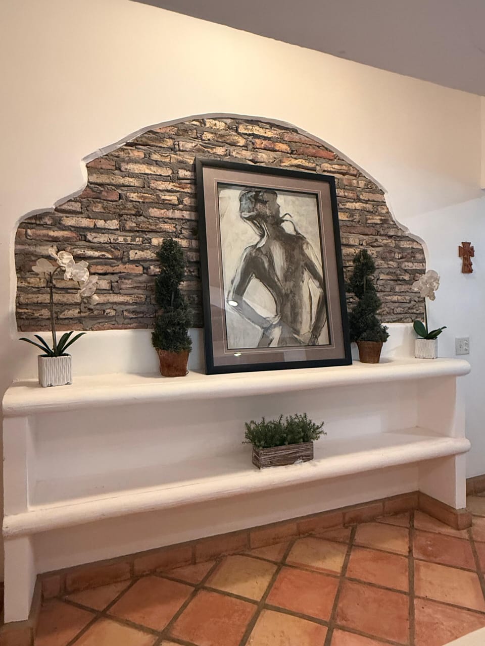 A detailed interior view of a white hallway display shelf decorated with potted plants, set against a striking rustic brick accent wall with framed artwork.
