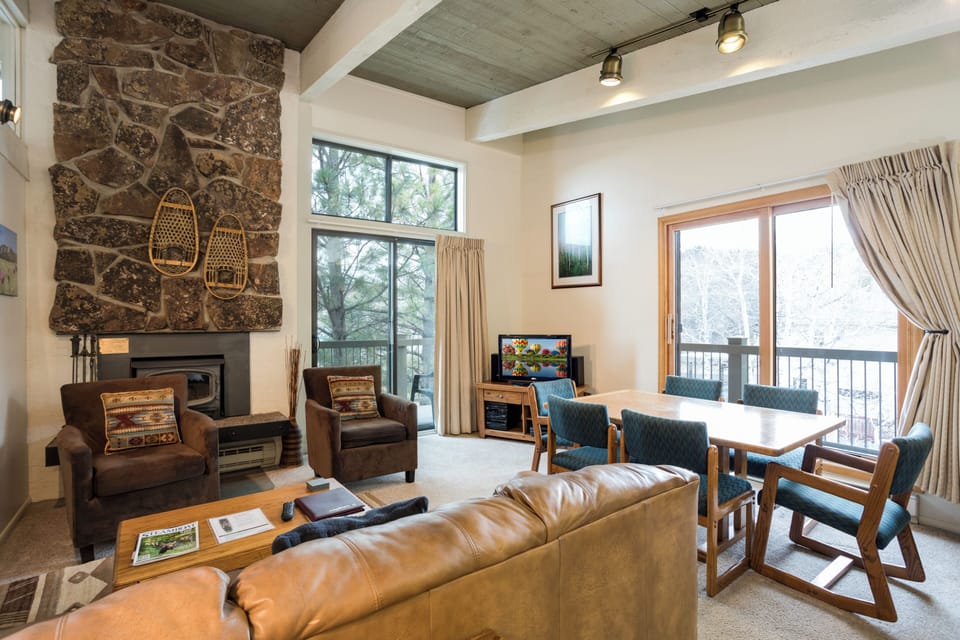 Unwind in your inviting living space with a dramatic stone fireplace and mountain views through expansive windows, where cozy seating and a dining area create the perfect retreat after a day of adventure.