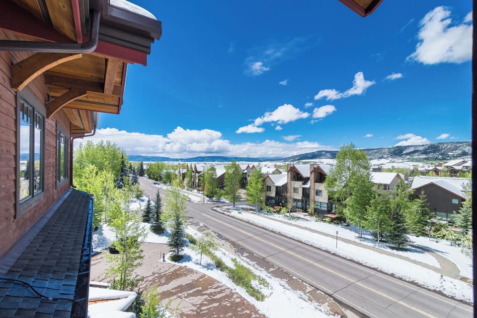 A mountain community showcasing tree-lined streets and residential neighborhoods beneath a vivid blue sky, with distant snow-dusted peaks framing the scenic surroundings.