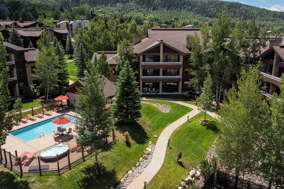Aerial view of the property nestled among trees and mountains, with swimming pool and hot tub amenities on beautifully landscaped grounds.