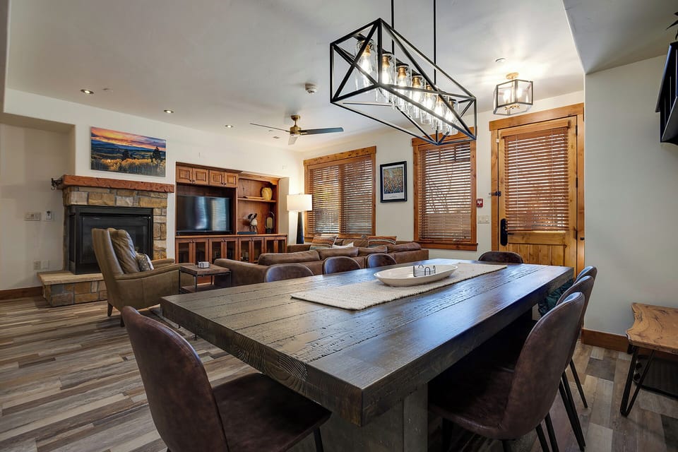 Gather around a grand dining table under statement lighting, with a cozy stone fireplace, plush seating, and mountain-inspired décor creating your perfect base for memorable stays.