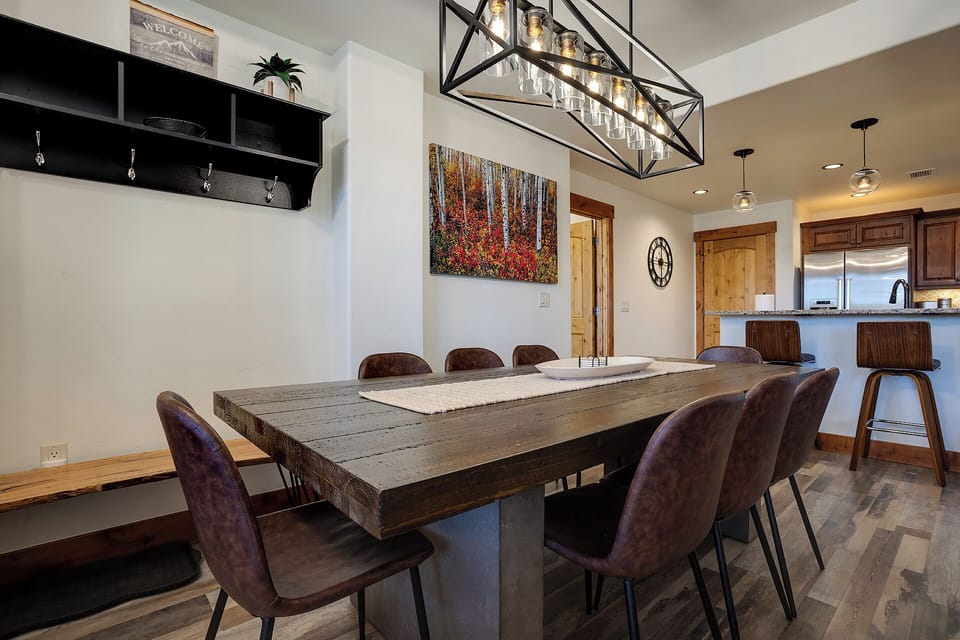 Gather around this stunning rustic dining table where your group can share meals and stories beneath a striking chandelier. The open layout flows into a modern kitchen, perfect for preparing feasts together.