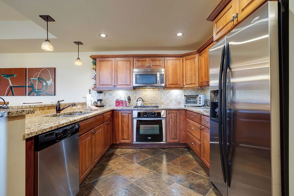 Your gourmet kitchen features warm wood cabinetry, granite counters, stainless steel appliances, and tile backsplash—perfectly equipped for preparing meals during your stay.