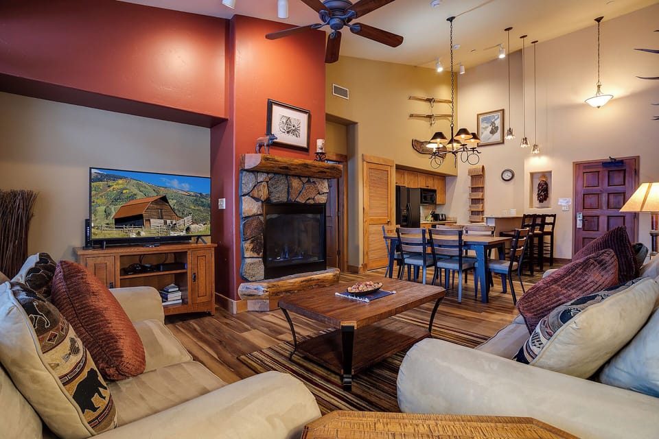 Unwind in your spacious living area featuring plush sofas, a stone fireplace, and an open-concept layout connecting seamlessly to your fully equipped kitchen and dining space.