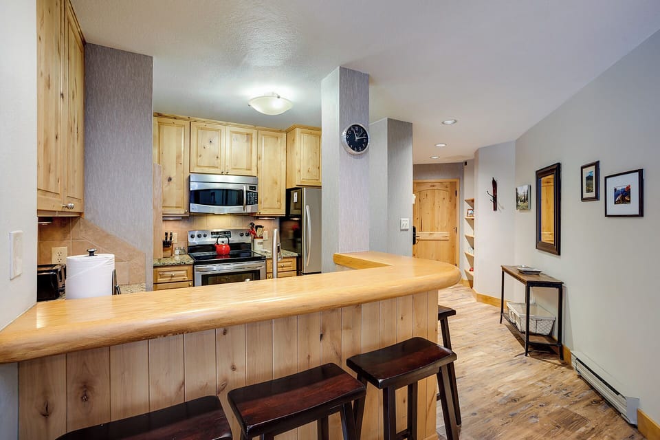 Your mountain retreat features a fully equipped kitchen with warm wood cabinetry, stainless steel appliances, and a curved breakfast bar—perfect for cozy meals and morning coffee before your adventures.