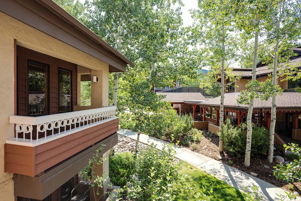 The property features two contemporary buildings set around a beautifully landscaped courtyard with mature trees, garden beds, and pathways, creating a peaceful mountain retreat atmosphere.
