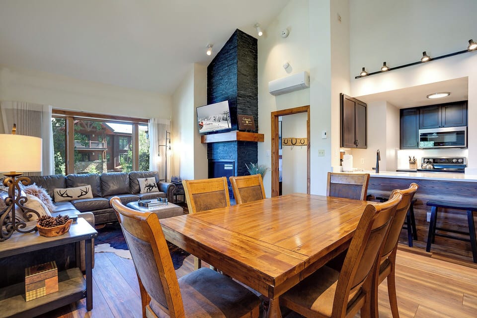 Gather with loved ones in your open-concept living area, where a stunning floor-to-ceiling fireplace anchors the space and natural light floods through large windows, creating a warm and inviting alpine retreat.