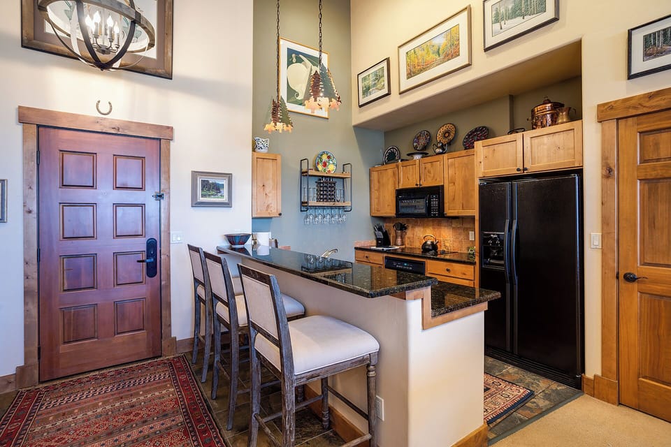 Step into your mountain home where rustic wood meets modern convenience. Your fully equipped kitchen features granite countertops, sleek black appliances, and charming pendant lighting—perfect for preparing meals after a day exploring the slopes.