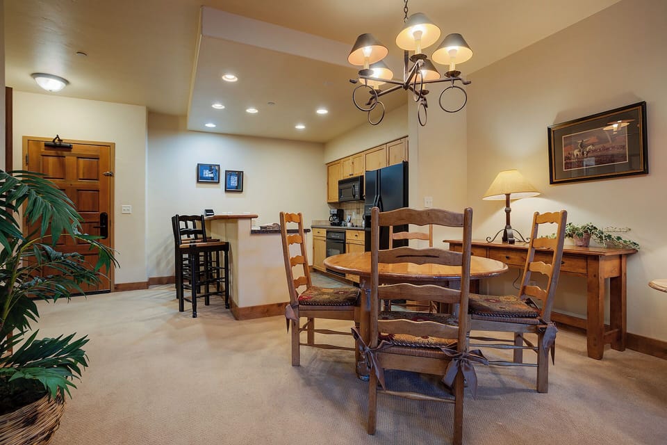 Gather around the rustic wooden dining table, where memorable meals and conversations await under warm lighting. The fully equipped kitchen sits ready for your culinary adventures.
