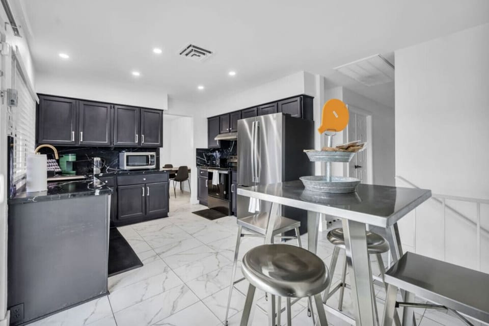 Modern kitchen with sleek black cabinetry, Samsung stainless steel French door fridge, Frigidaire electric range, Keurig coffee maker, and a compact 4-seat metal breakfast bar—perfect for morning brews or quick bites.
