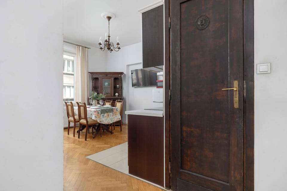 A hallway view reveals a dark wooden door leading to another room. The dining area is visible in the background, illustrating the apartment's open layout.