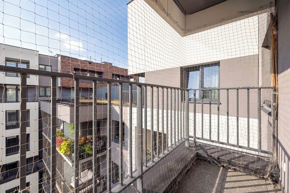 The balcony viewpoint displays the metal railing and protective netting, capturing the modern residential architecture under a sunny sky.