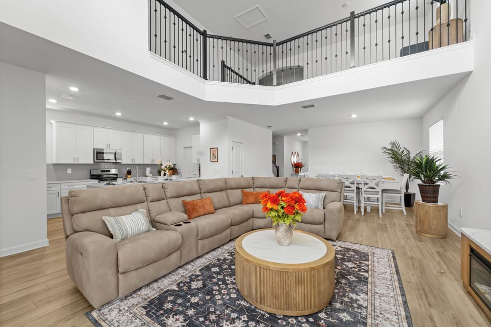 Relax in your spacious living area with soaring ceilings and a balcony overlooking the open floor plan. The plush sectional invites you to unwind, while the bright kitchen and dining space make gathering effortless.
