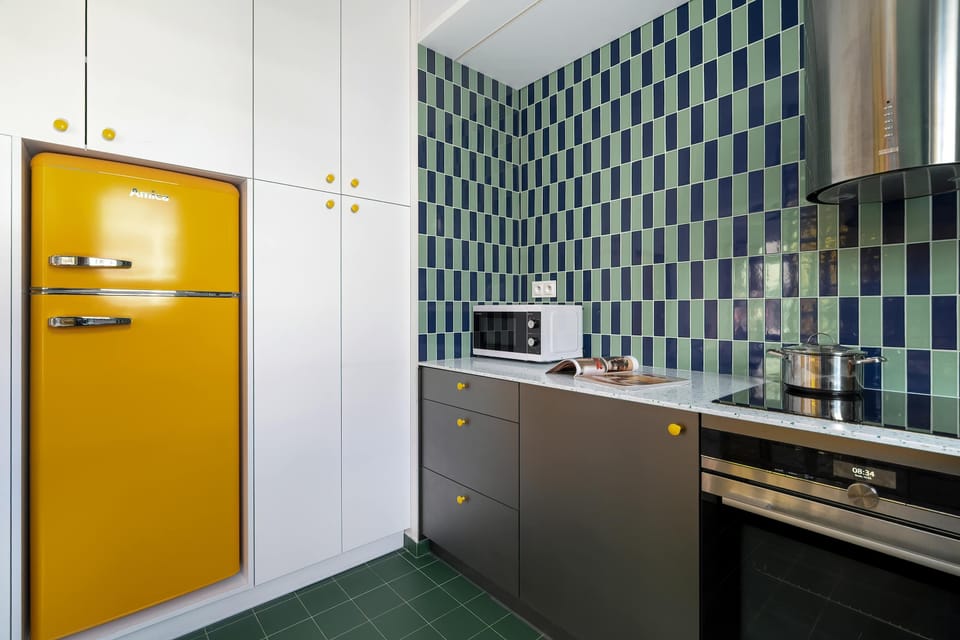Compact kitchenette features dark cabinets, colorful details, and modern appliances.