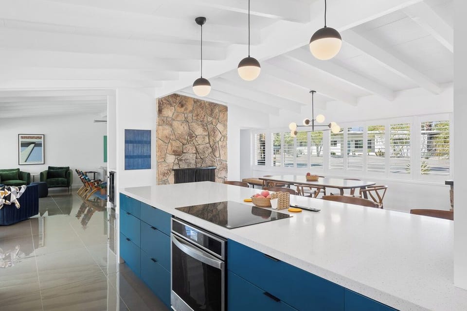 Cook and connect in this stunning open-plan space where sleek blue cabinetry meets warm stone fireplace accents.