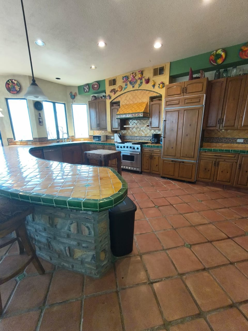 A spacious kitchen featuring a curved green talavera-tiled counter, stainless steel range, and abundant custom wood cabinetry.