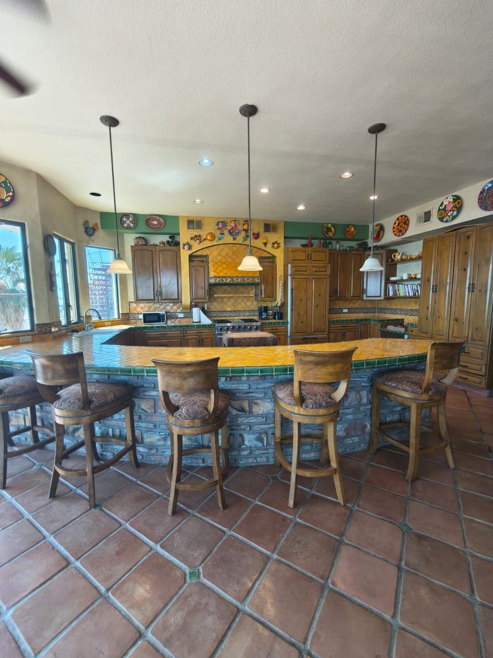 A vibrant kitchen featuring a curved green talavera-tiled breakfast bar, wood cabinetry, and colorful decorative plates lining the walls.