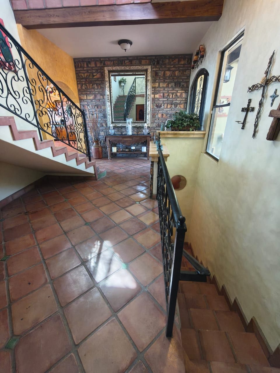 A grand staircase featuring terracotta tile steps, wrought iron railings, and a decorative console table with religious artwork.