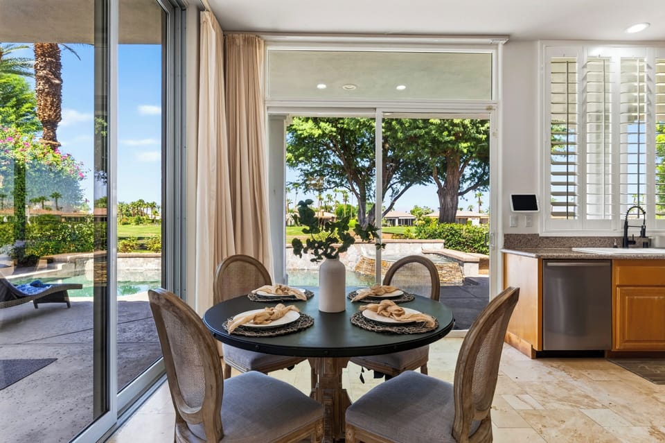 Round dining table sits beside expansive glass doors overlooking the landscaped patio.