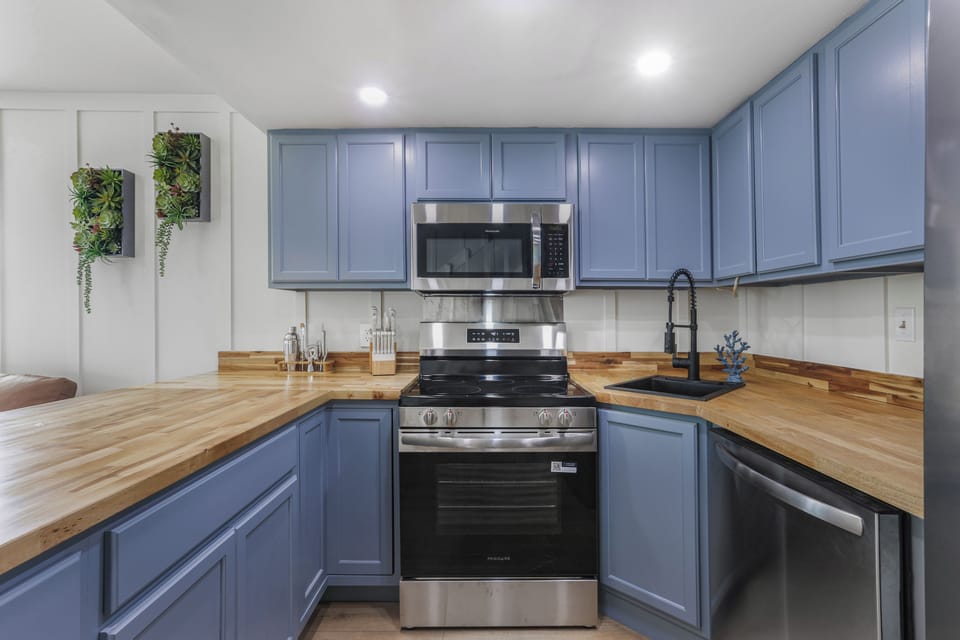 Stylish blue kitchen with butcher block counters and stainless appliances
