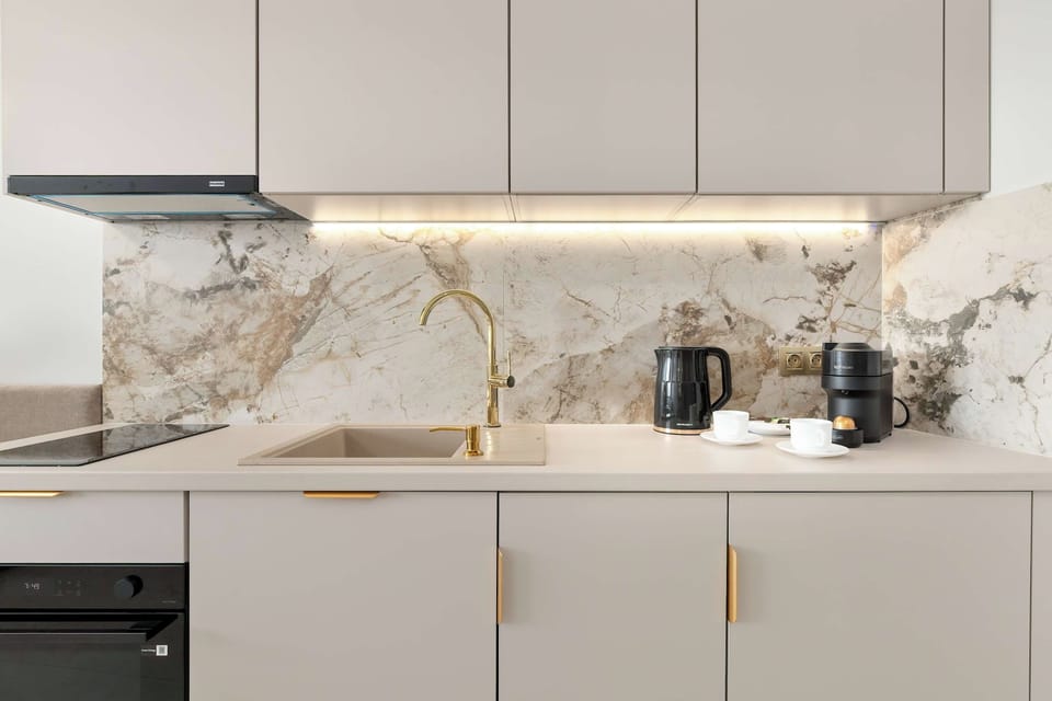 A modern kitchenette with white cabinets, marble backsplash, and built-in appliances.