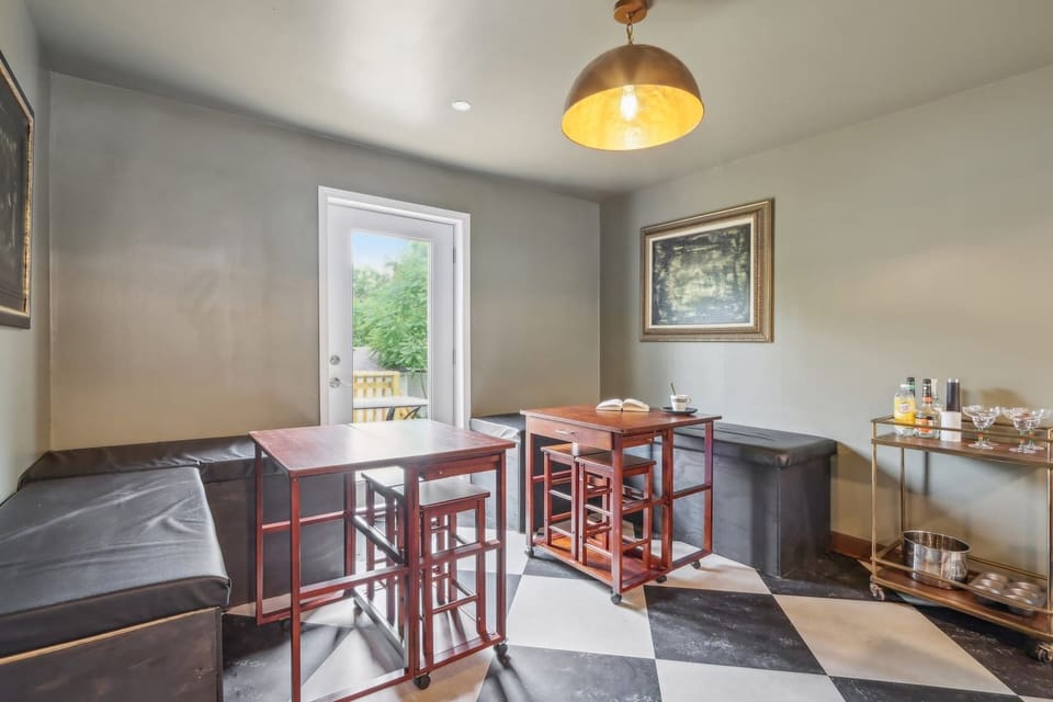 Two bar-height dining tables with stools, seating areas, and a door opening. 