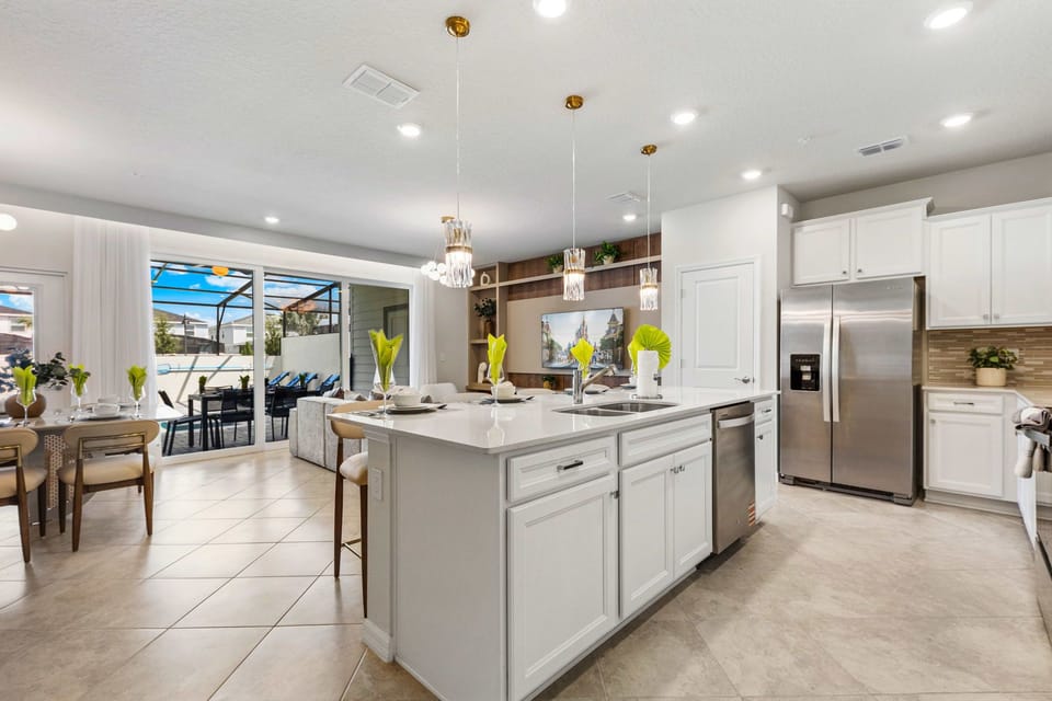 Gather in this bright open-concept kitchen and living area, featuring a large island, stainless steel appliances, and seamless access to the pool patio.