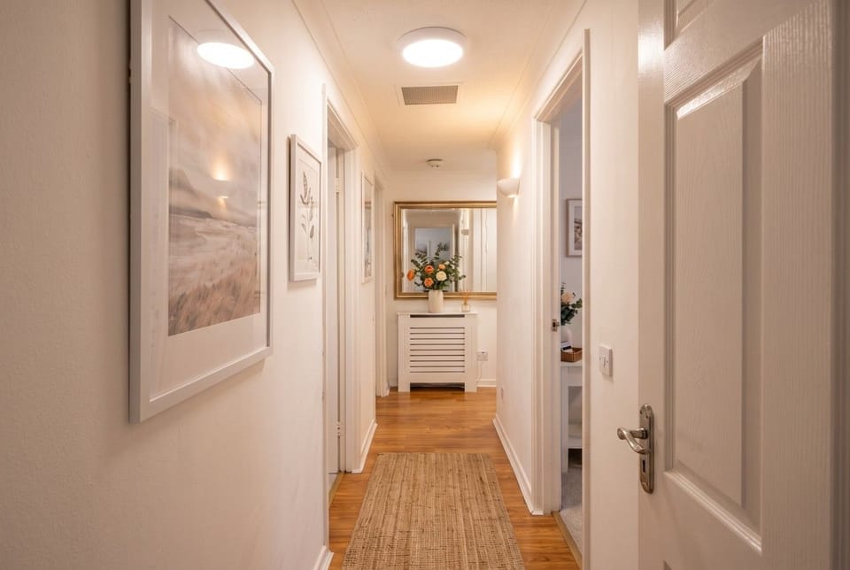 The hallway runs past framed prints toward a mirror at the far end.