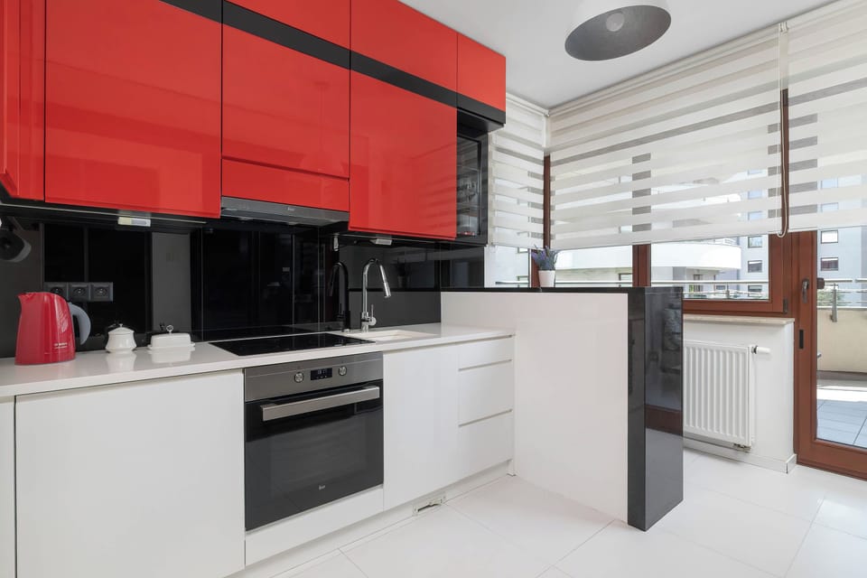 A modern kitchen with white cabinets, a black countertop, and distinctive red upper cabinets. The space is well equipped and offers a practical setting for preparing meals.