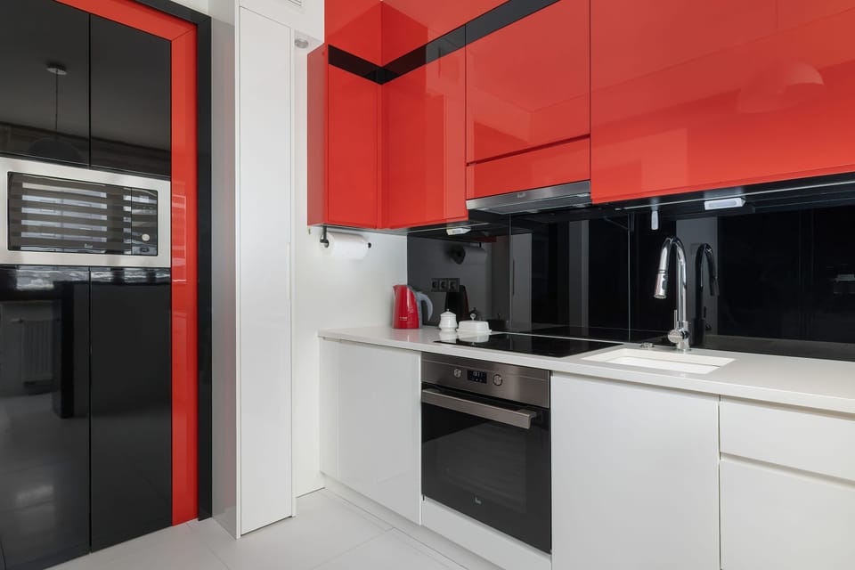 A modern kitchen featuring white cabinets, a black countertop, and red upper cabinets. Built in appliances and ample storage make the space practical for everyday cooking.