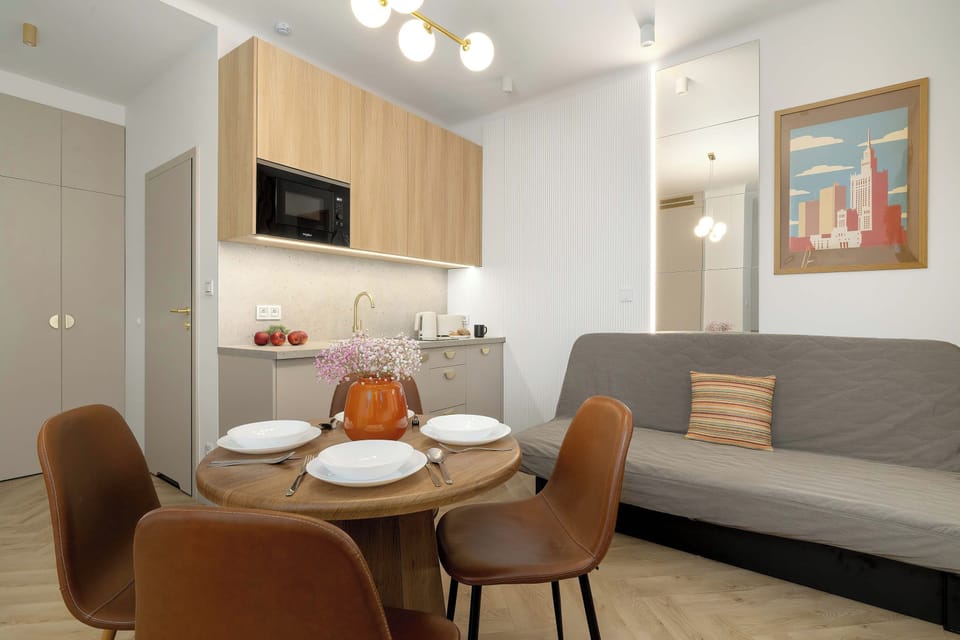 A round dining table is set with plates and surrounded by modern chairs. A grey couch and kitchen cabinets complete this open-concept room.