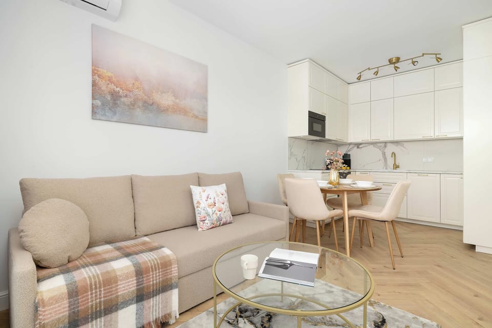 An open-concept living space seamlessly connects a cozy lounge area with a dining section. A beige sofa rests on the left, while a round dining table with comfortable chairs occupies the center.