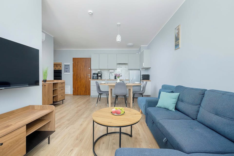 A spacious living room is centered around a prominent blue sectional sofa and a wooden coffee table. A flat-screen TV and a wooden media console sit against the opposite wall.
